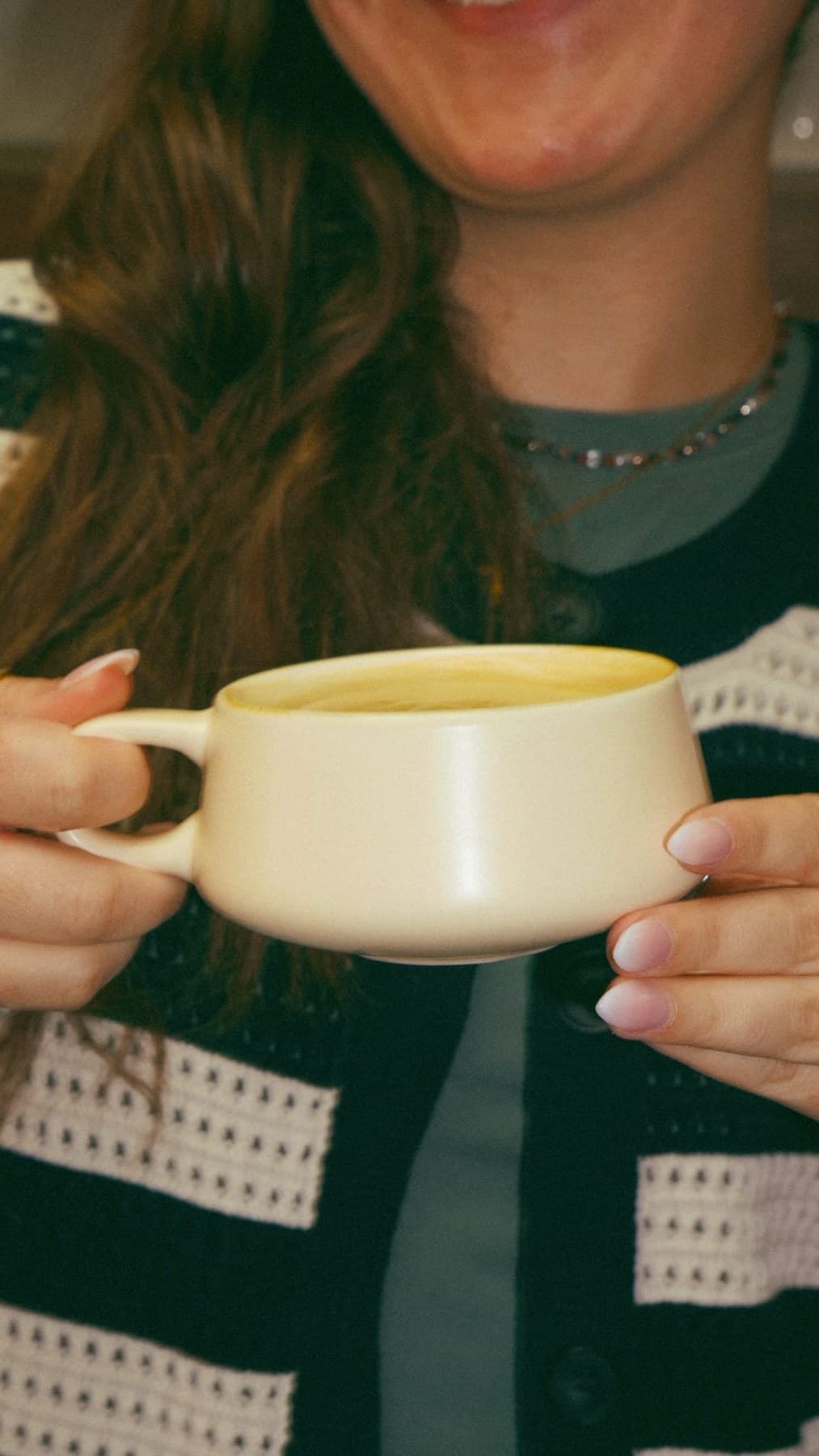 Two hands lifting coffee mugs at a wooden table at Revival Coffee