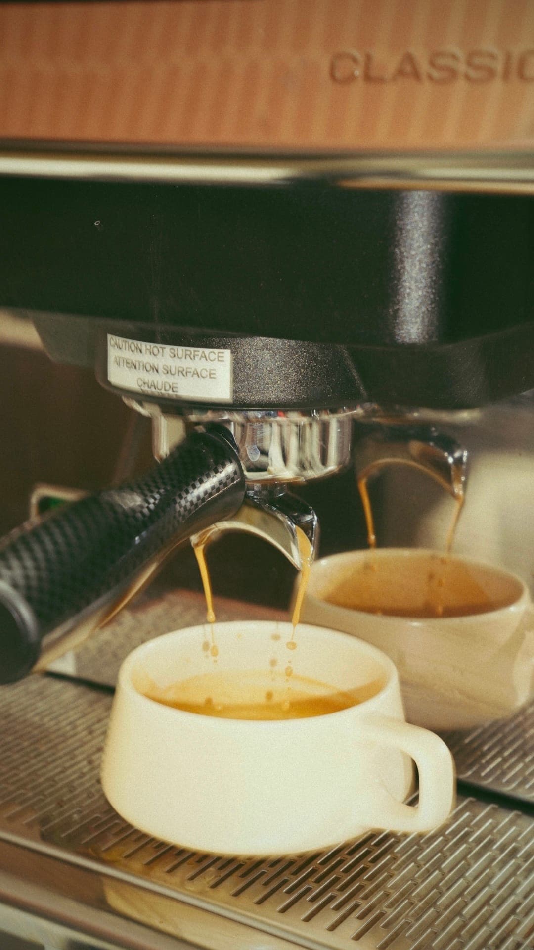 Barista hands pulling espresso shots on a chrome machine in morning light