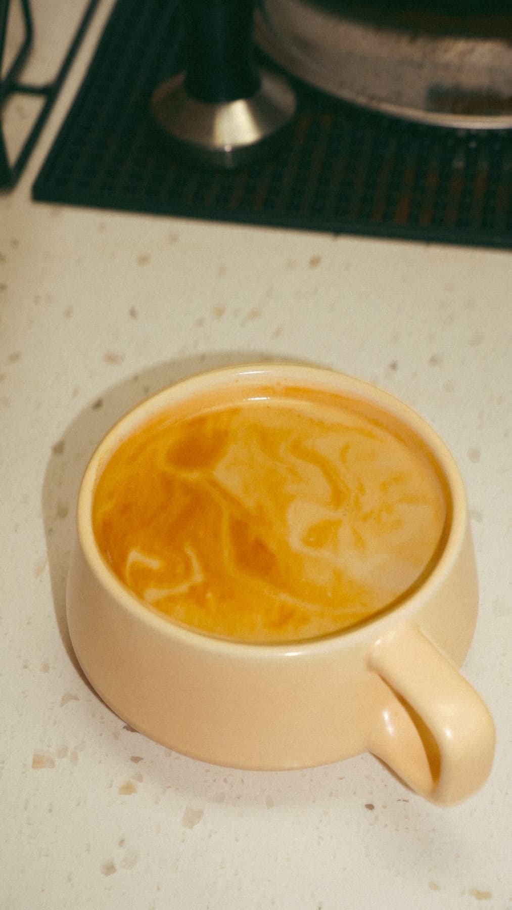 Hand pouring latte art into a ceramic mug on a warm wood counter